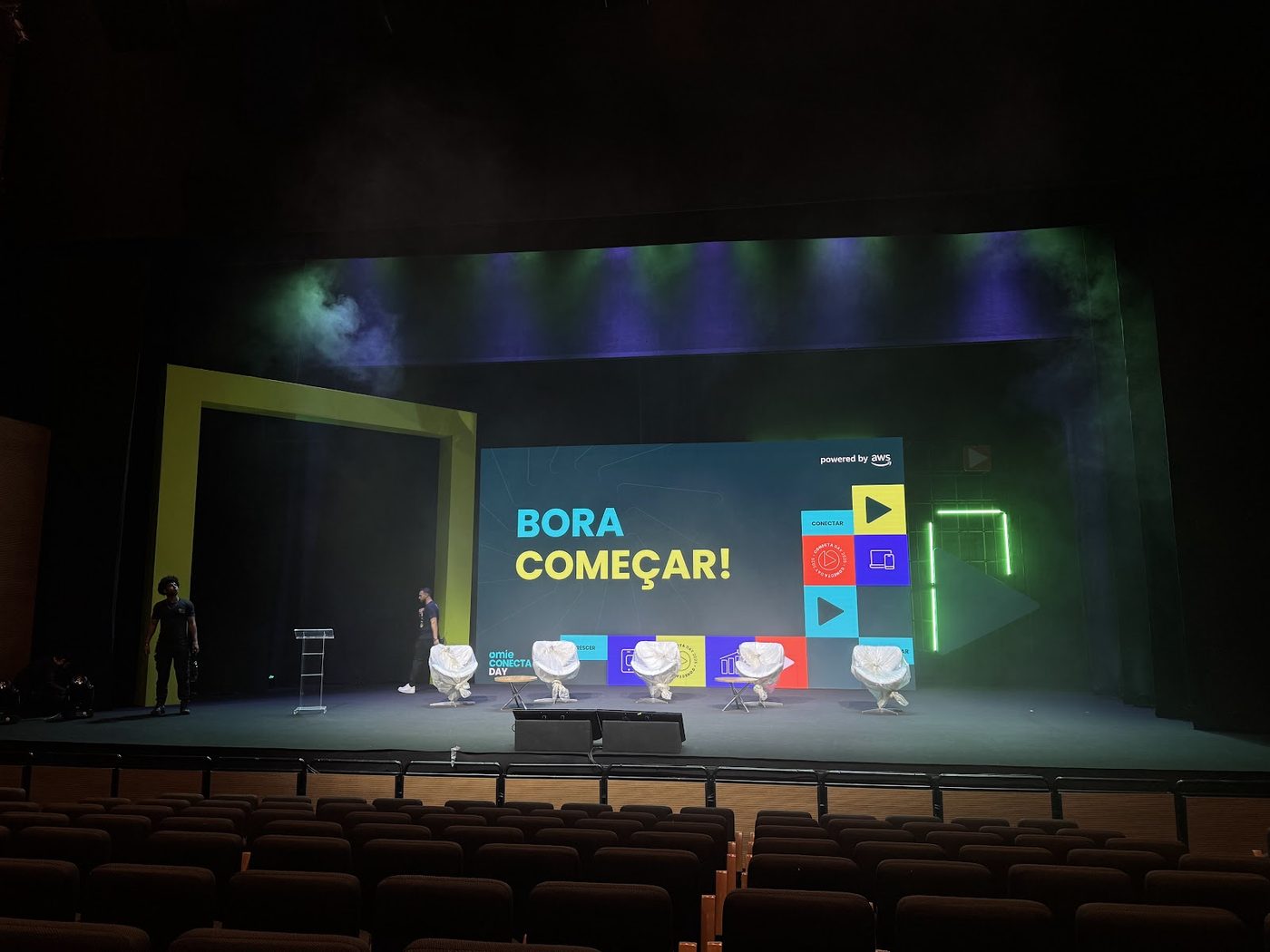 Mesa de operação técnica com palco e telão LED ao fundo em evento corporativo