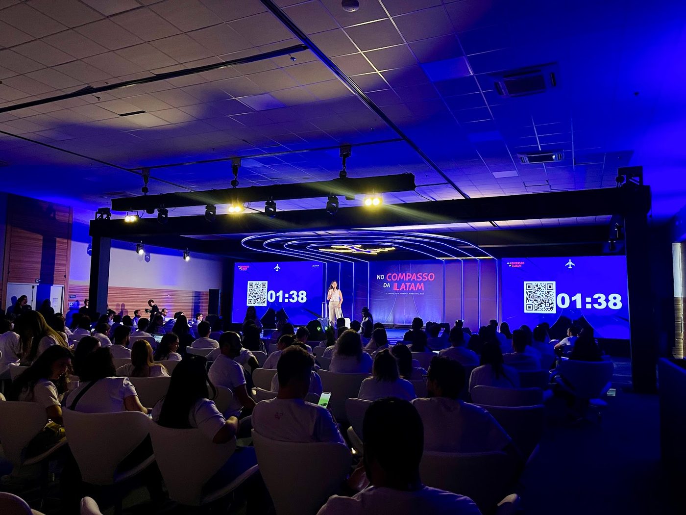 Palco corporativo com arcos de LED e iluminação cênica em tons de azul e roxo