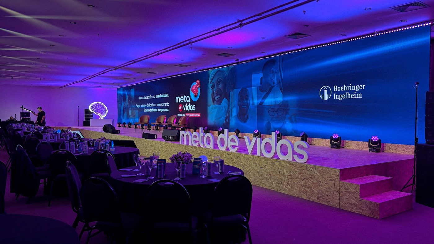 Painel LED cobrindo parede inteira de salão corporativo com cenografia 3D e mesas postas