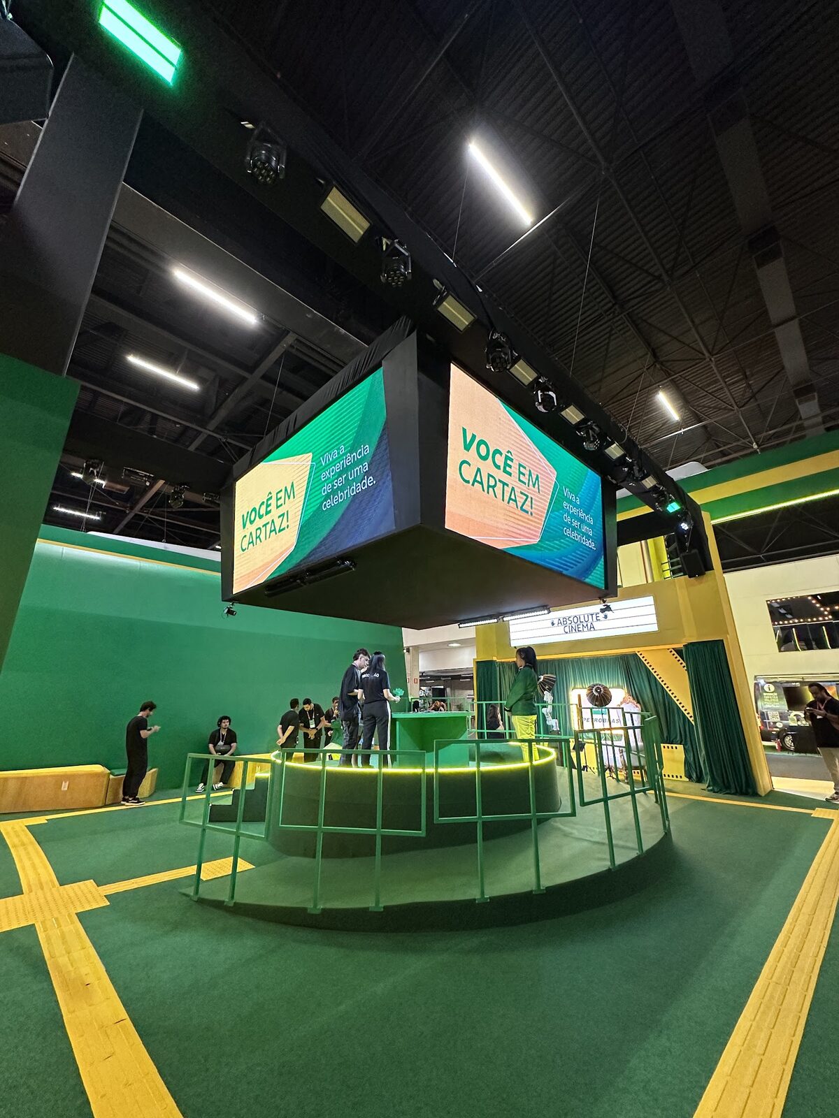 Painel LED em formato de cubo suspenso sobre estande corporativo em feira de negócios