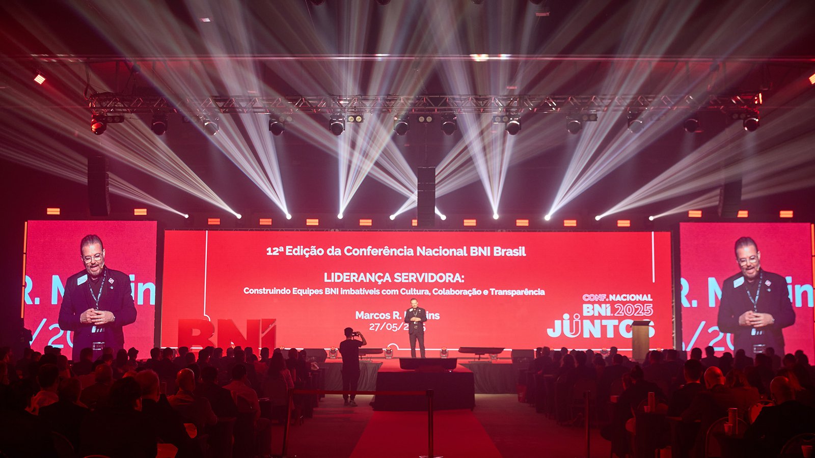 Palestrante em palco de convenção corporativa com setup audiovisual profissional e teleprompter presidencial
