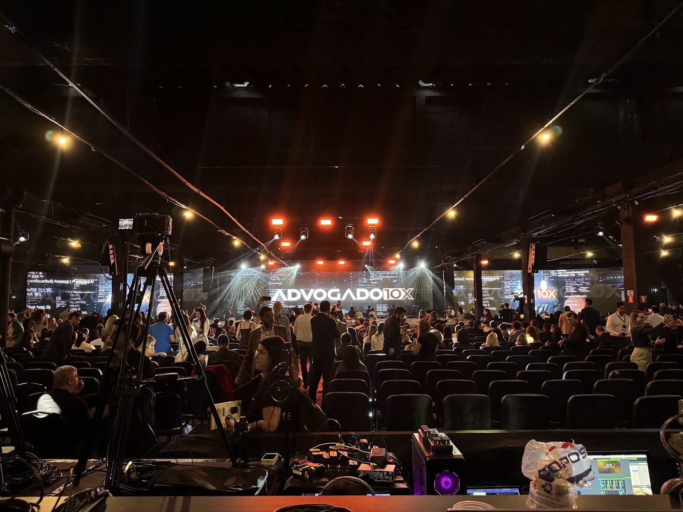 Palco corporativo com feixes de luz coloridos e plateia em pé durante convenção de negócios