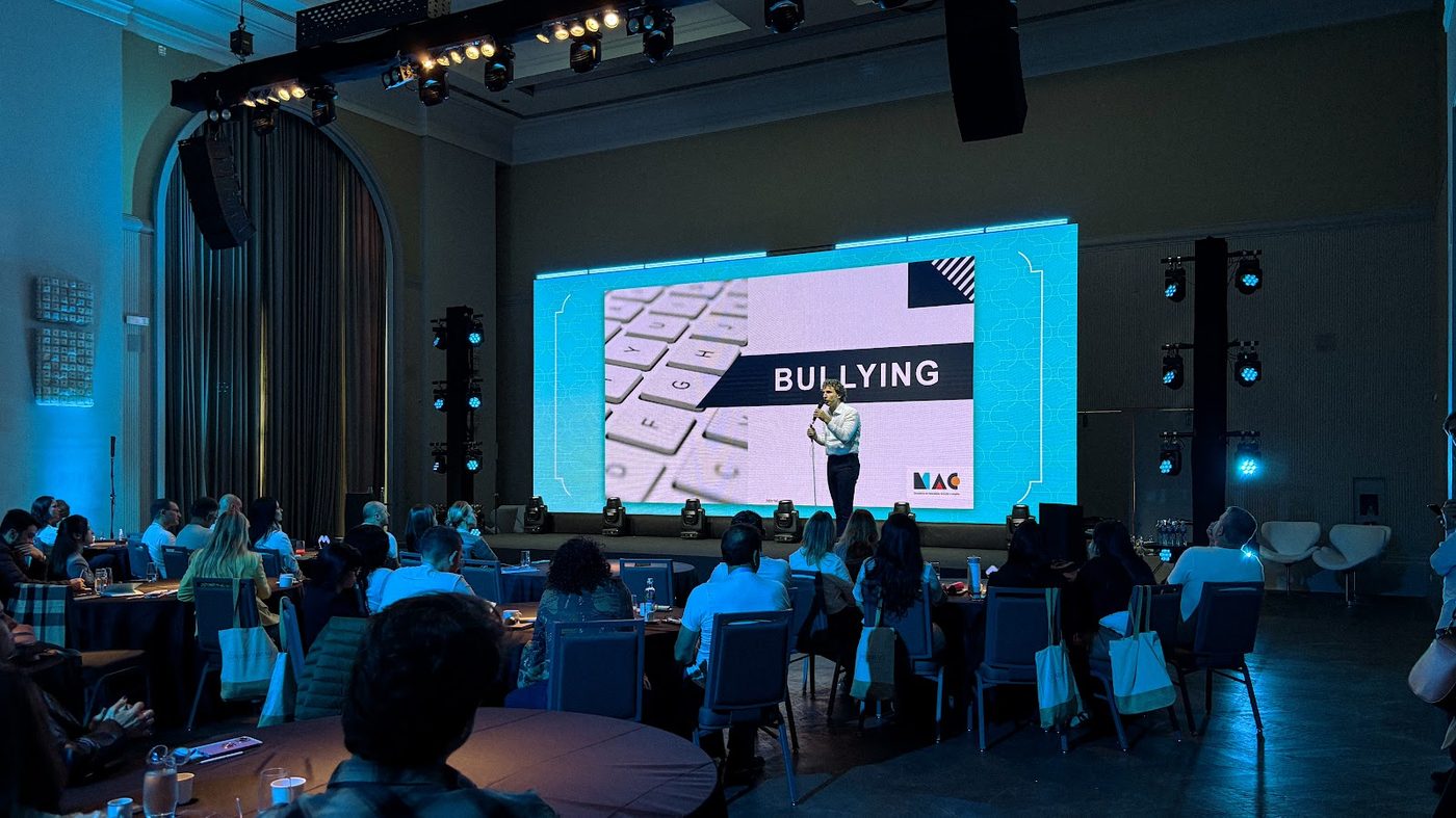 Convenção corporativa com painel de LED azul, sonorização e plateia em mesas redondas