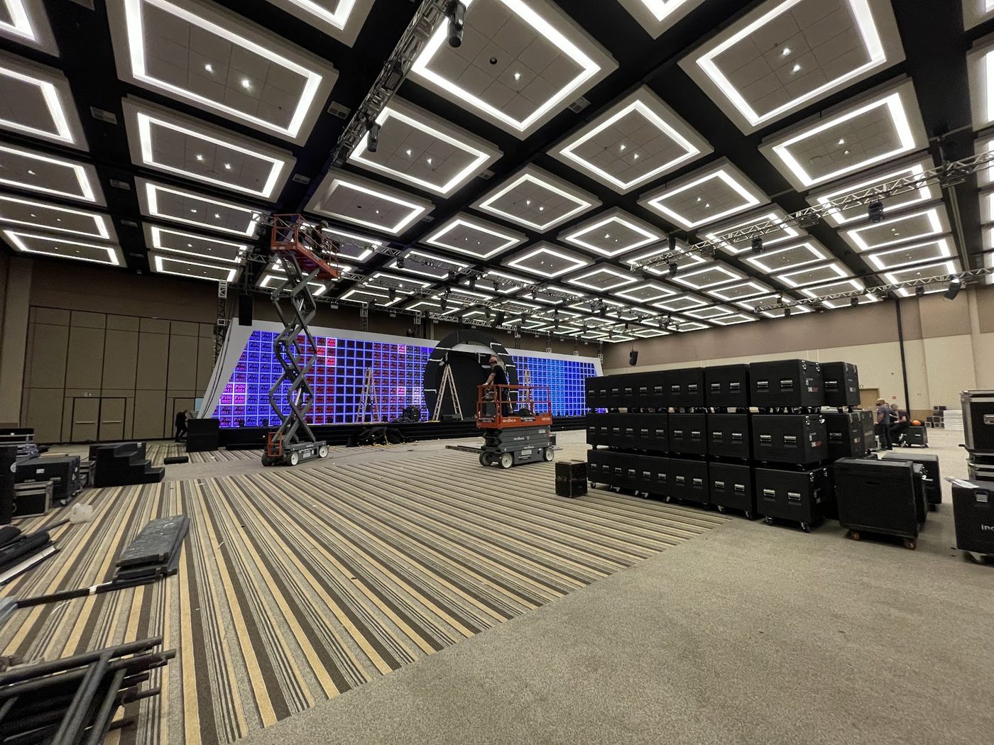 Palco de evento corporativo com iluminação cênica, câmeras de transmissão e plateia ao fundo
