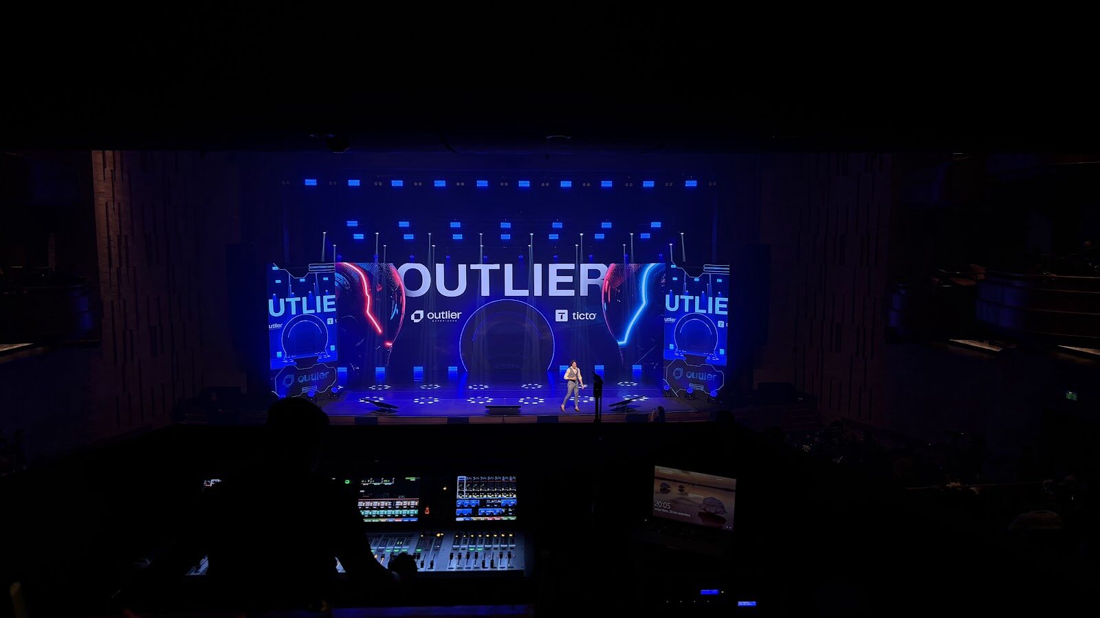Mesa de operação técnica com visão do palco e telão LED em evento corporativo