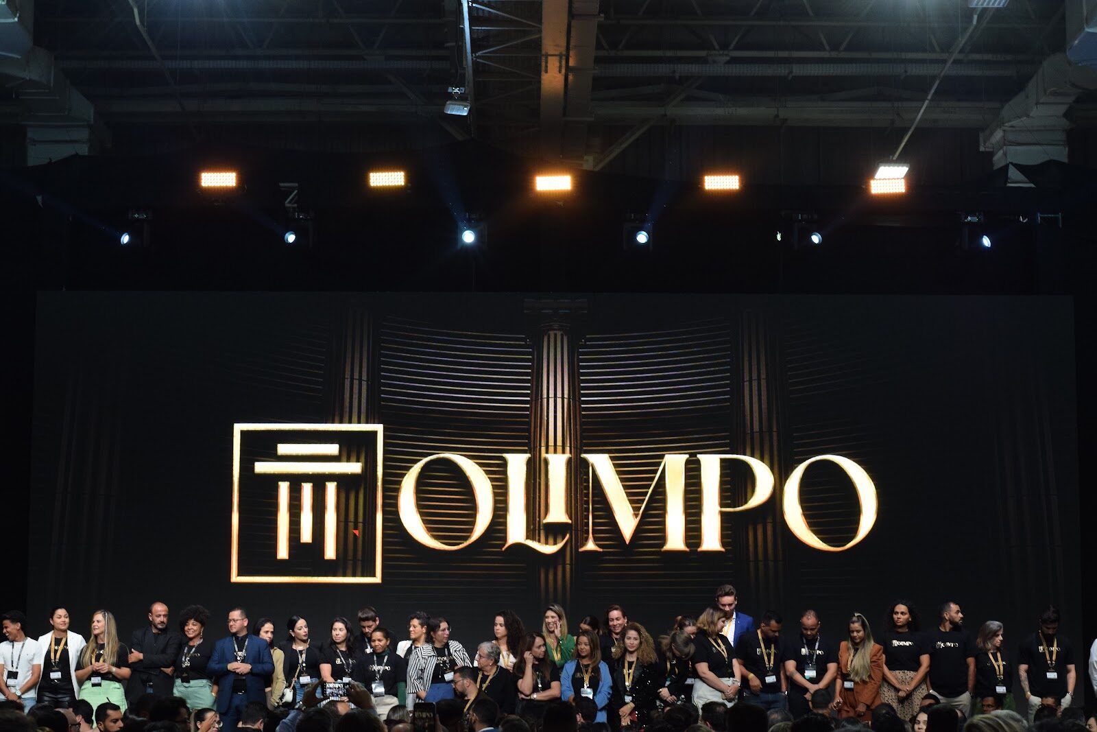 Premiados em palco com cenografia dourada e iluminação cênica em evento corporativo
