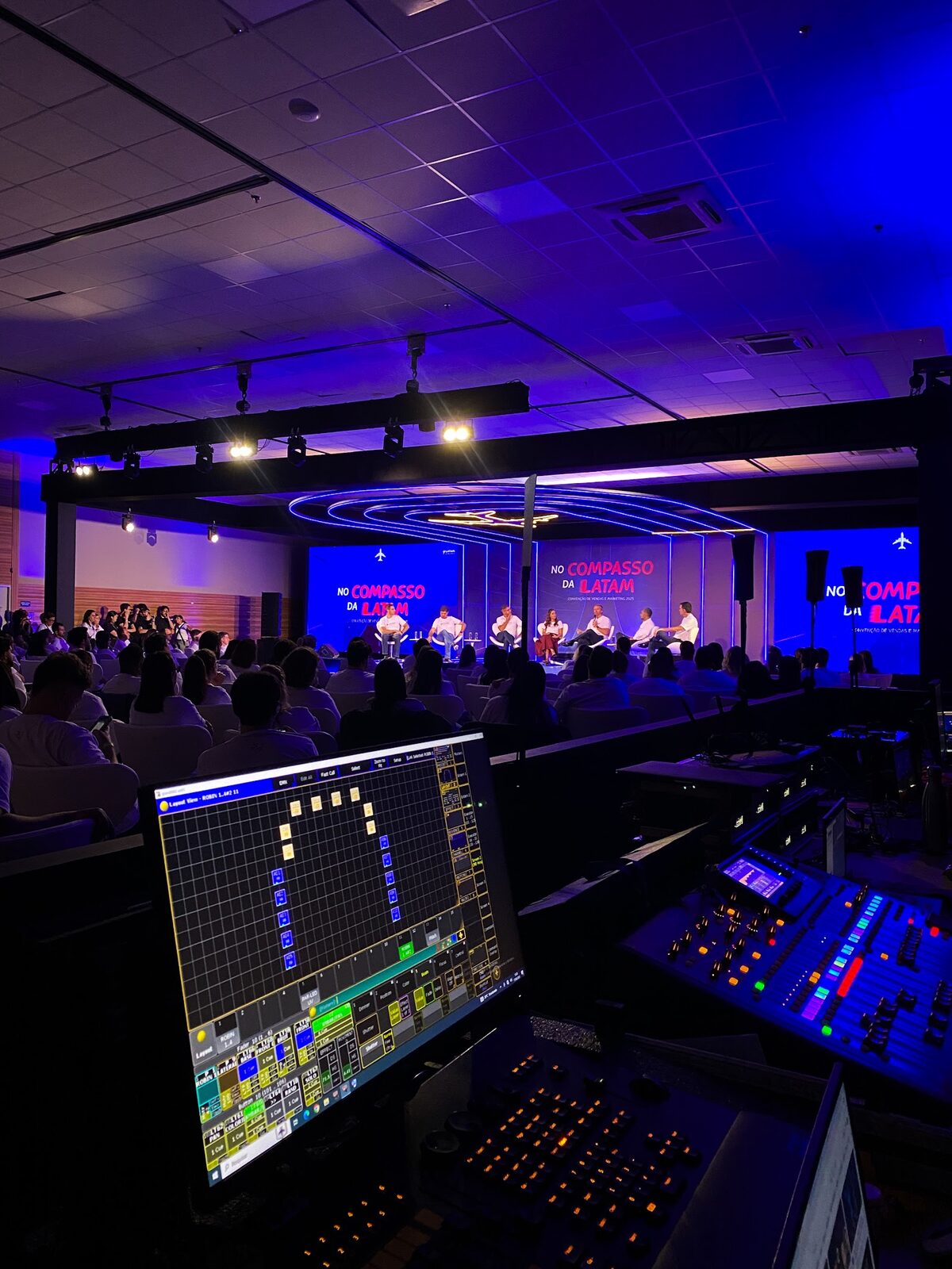 Mesa de controle técnico operando palco com telões de LED e plateia ao fundo