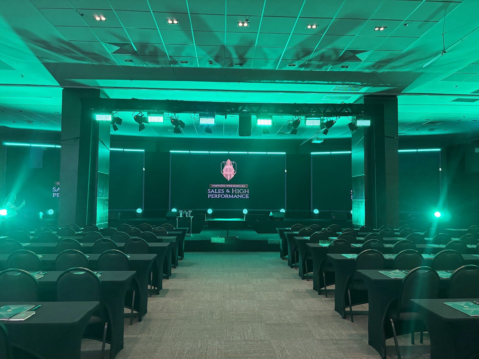 Sala de evento com iluminação de ambientação verde turquesa e mesas simétricas