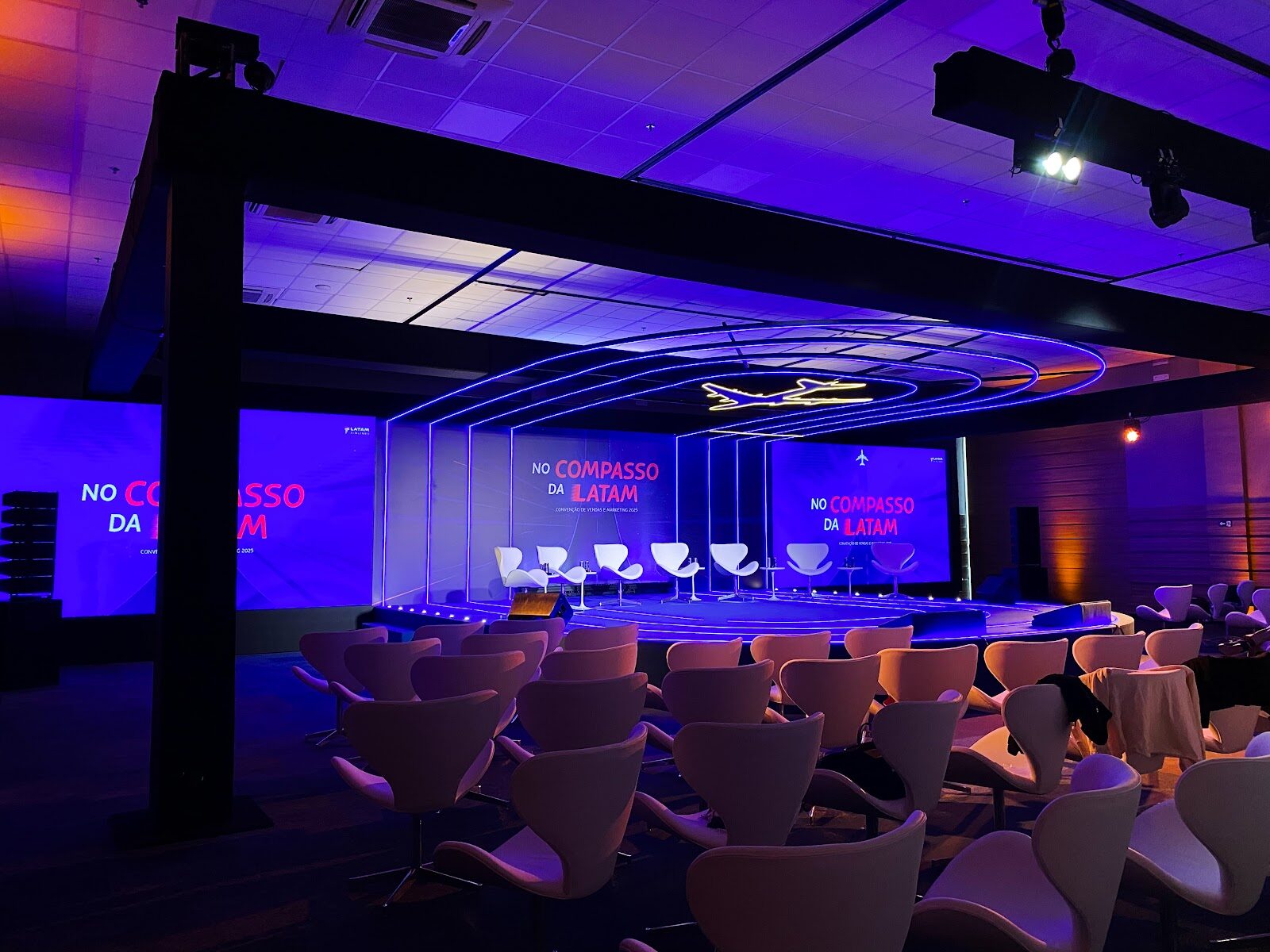 Cenografia corporativa com arcos de LED e ambientação em azul e roxo em palco vazio antes do evento